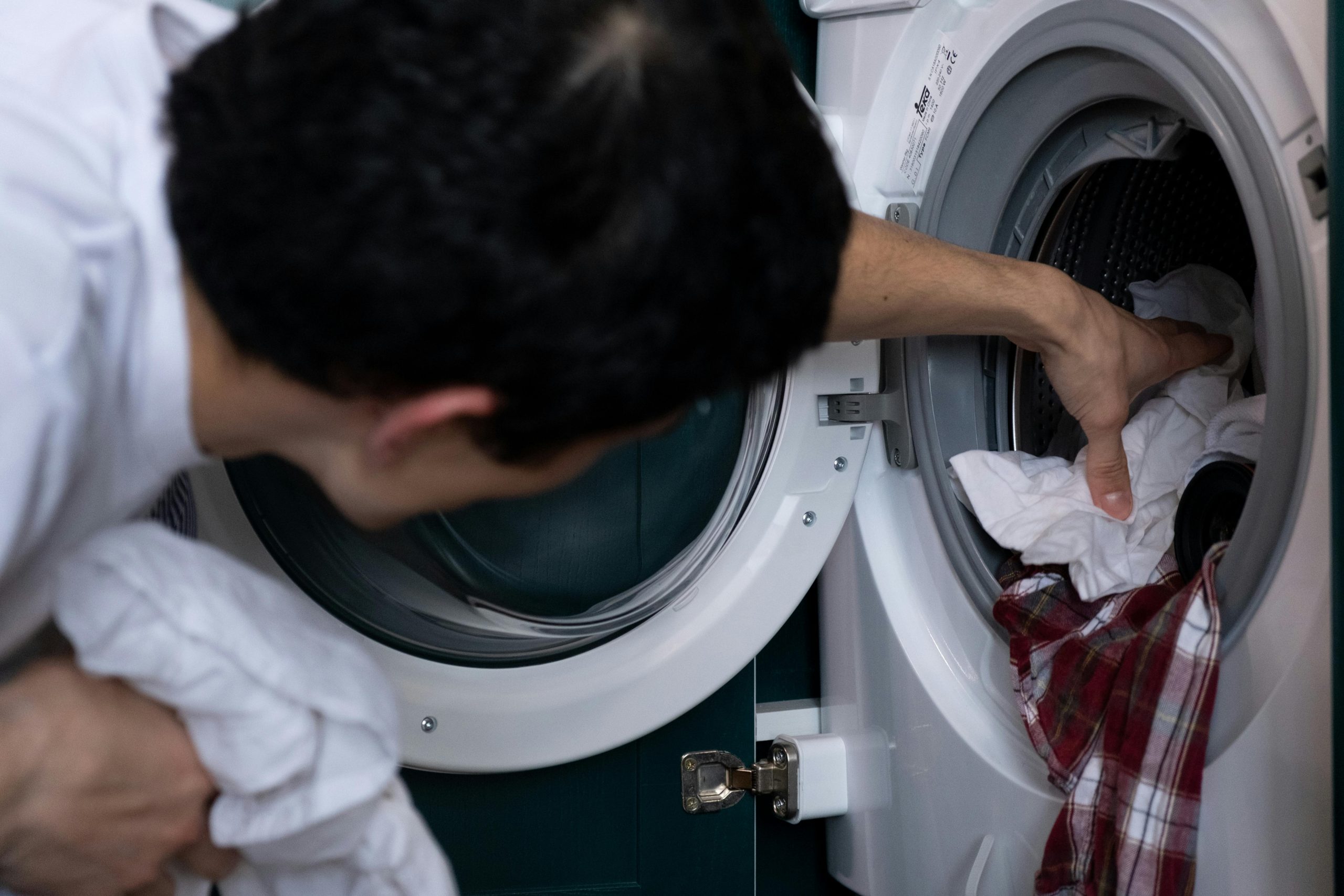 Home Close-up of a man placing clothes into a washing machine during household chores.